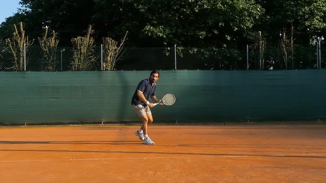 male tennis player hitting ball backhand slow motion on a red clay court professional