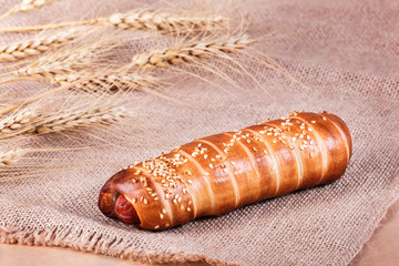 Hot dog with sesame seeds on rustic background with spikelets. Pastries and bread in a bakery