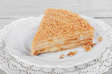 Cake Napoleon with sour cream and walnuts on plate, on a light wooden background. Selective focus