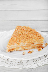 Cake Napoleon with sour cream and walnuts on plate, on a light wooden background. Selective focus