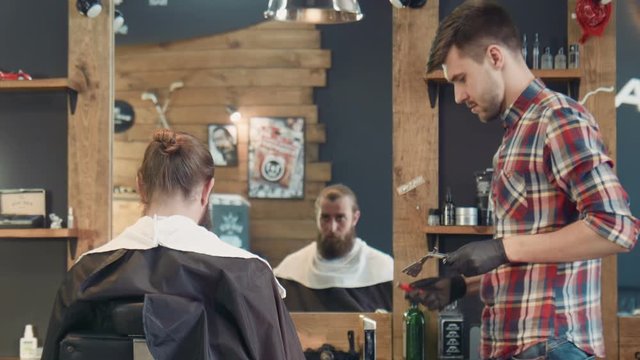 Side view of professional young barber spraying razor with fragrance and sets fire. Antiseptic method of cleaning of the razor
