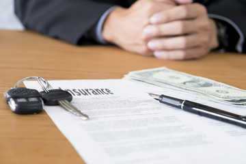 closeup of a pen with car key, money to pay for car insurance.