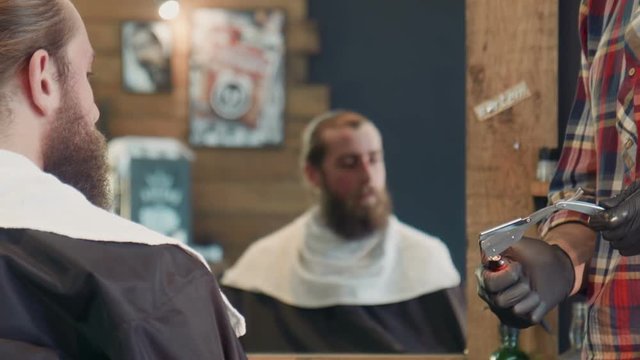 Side view of professional young barber spraying razor with fragrance and sets fire. Antiseptic method of cleaning of the razor