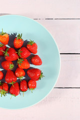 Ripe red strawberries on a blue ceramic plate and pink wooden background