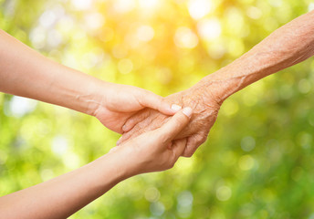 Senior and young women holding hands on abstract nature background and color tone effect.