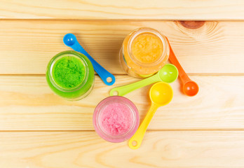 Three jars  different baby puree, spoon on  background  light wood.