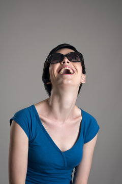 Laughing young short hair cutie wearing sunglasses over gray studio background.