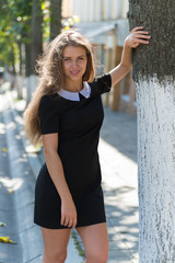 Portrait of glamorous girl in black dress standing near tree
