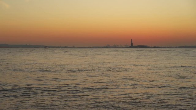 Statue of Liberty in the distance across Hudson River at evening hours sunset.
