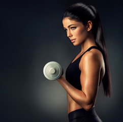 Beautiful fitness woman lifting dumbbells . Fitness sporty woman showing her well trained body . A beautiful girl's body with rippling muscles from strength training . 