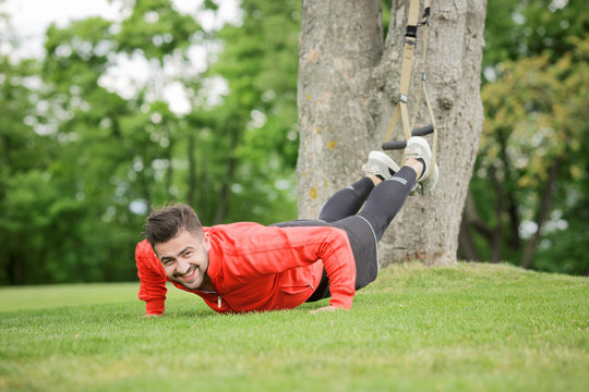 Picture of sport man training in park and smiling for camera. Happy fitness trainer preparing for competitions concerning jogging in green park.