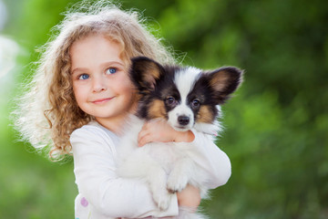 Little curly girl with a papillon puppy, outdoor summer