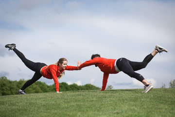 Sport man and woman in red jackets training in green park or forest. Couple of fitness people doing sport exercises outdoors.