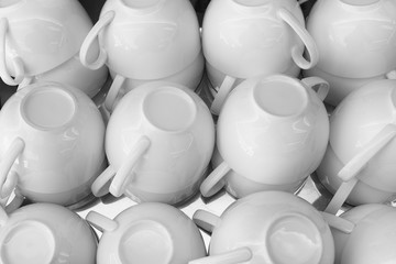 the stack of the white cups of tea in the shelf, the white tea cups on the table in black and white tone