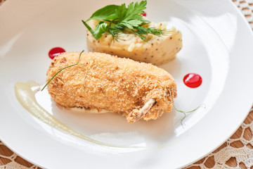 Chicken Kiev fried in breadcrumbs, Parmesan sauce and mashed potatoes with Dijon mustard served on a white plate