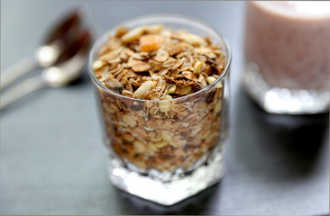 Granola is for the breakfast in the transparent glass with yogurt, napkins and spoons on the grey background