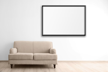 Cozy couch and empty picture frame on wall background