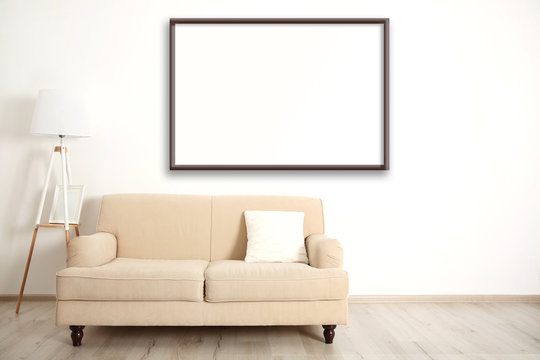 Beige couch with lamp and empty picture frame on wall background