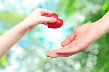 Heart in child and mother hands on green nature background. Concept of taking care, protection, helping and assistance