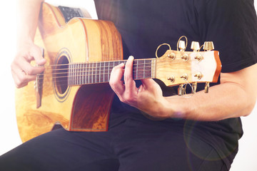 Young man playing on acoustic guitar on light background