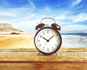 Summer time concept. Alarm clock on wooden table on beach background
