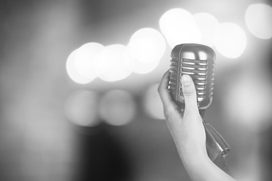 Retro microphone in female hand on abstract blurred background
