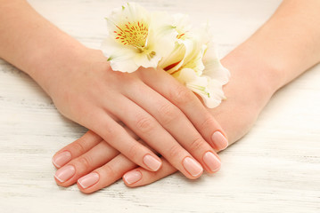 Obraz na płótnie Canvas Spa concept. Woman hands with beautiful flowers and nail polish on wooden background, close up