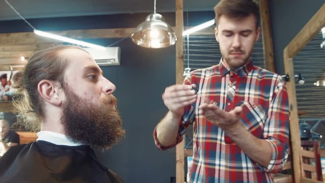 Professional barber smearing oil over client's beard