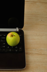 A green apple displayed with a notebook and coloring pencils on a laptop