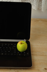 A green apple displayed with a notebook and coloring pencils on a laptop
