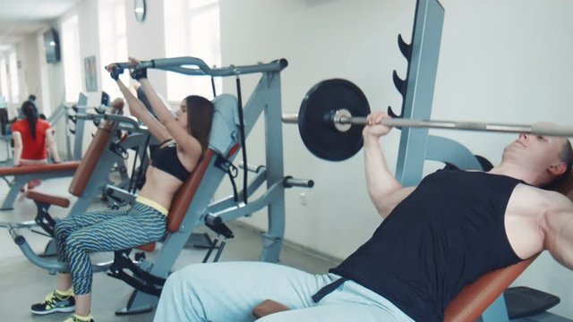 Couple doing bench press. Man drinking water then continues to exercise