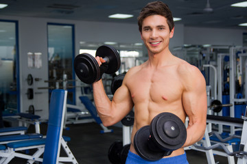 Fototapeta na wymiar Young smiling athlete lifting weights in the gym