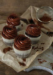 Chocolate cupcakes on baker paper over wooden background