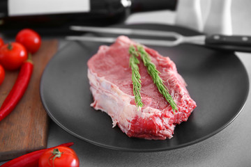 Raw pork steak with meat fork and rosemary on black plate