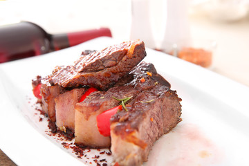 Sliced roasted pork steak with bottle of red wine on white plate