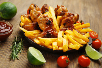 Baked chicken wings with French fries on wooden table