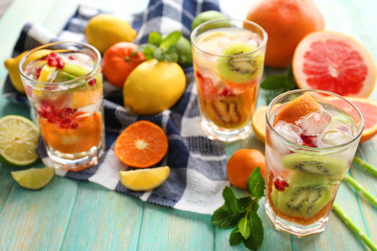 Refreshing cocktails with ice, mint, pomegranate seeds and slices of fruits on blue wooden background