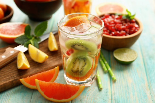 Refreshing cocktail with ice, mint, pomegranate seeds and slices of fruits on blue wooden background