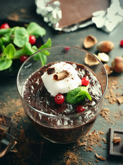 Glass cup of chocolate dessert with cranberries, fresh mint and frothed milk on black wooden table