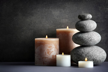 Fototapeta na wymiar Composition of spa pebbles and candles on grey background