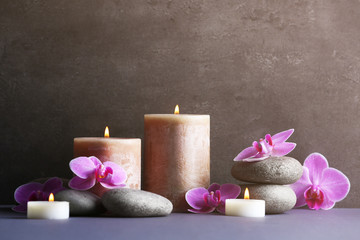 Fototapeta na wymiar Composition of spa pebbles, flowers and candles on grey background
