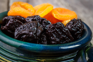 Organic prunes, dried plums and dried apricots in old tableware on rustic table