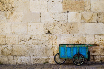 Old blue wooden cart. Wooden wheelbarrow standing near a stone wall. The old self-made wooden cart...