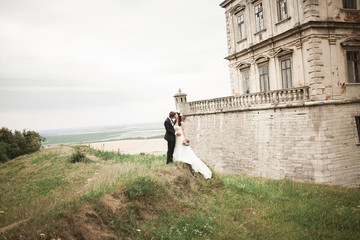Obraz premium Happy wedding couple hugging and kissing on background old castle