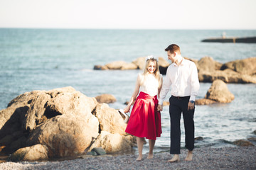 Romantic loving couple posing on stones near sea, blue sky