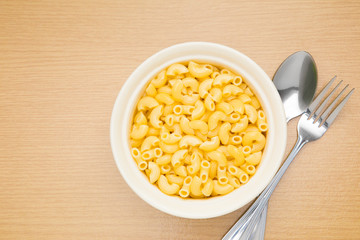 Macaroni in white bowl with spoon and folk on wooden table