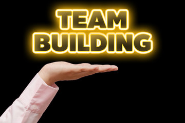 Business woman hand cupped holding the word TEAM BUILDING with orange yellow neon light