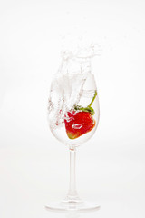 splashing strawberry into water glass on white background
