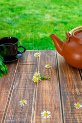 Brown teapot near black cup of tea on wooden with mint and chamomile table  in garden and on nature background. Tea concept. Closeup.