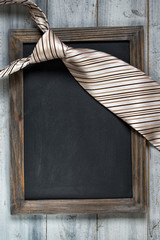 Fathers day concept, empty framed chalkboard and tie on wooden background